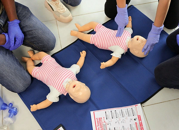Uczestnicy szkolenia Paediatric First Aid Course UK z manekinami do resuscytacji krążeniowo-oddechowej i ilustrowanym przewodnikiem krok po kroku.
